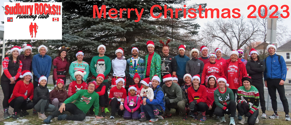A group of people wearing Santa hats and Christmas sweaters posing for a photo in front of a conifer tree. A group of people wearing Santa hats and Christmas sweaters posing for a photo in front of a conifer tree.