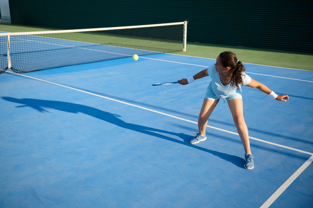 Une femme frappant une balle de tennis sur un terrain extérieur. Une femme frappant une balle de tennis sur un terrain extérieur.