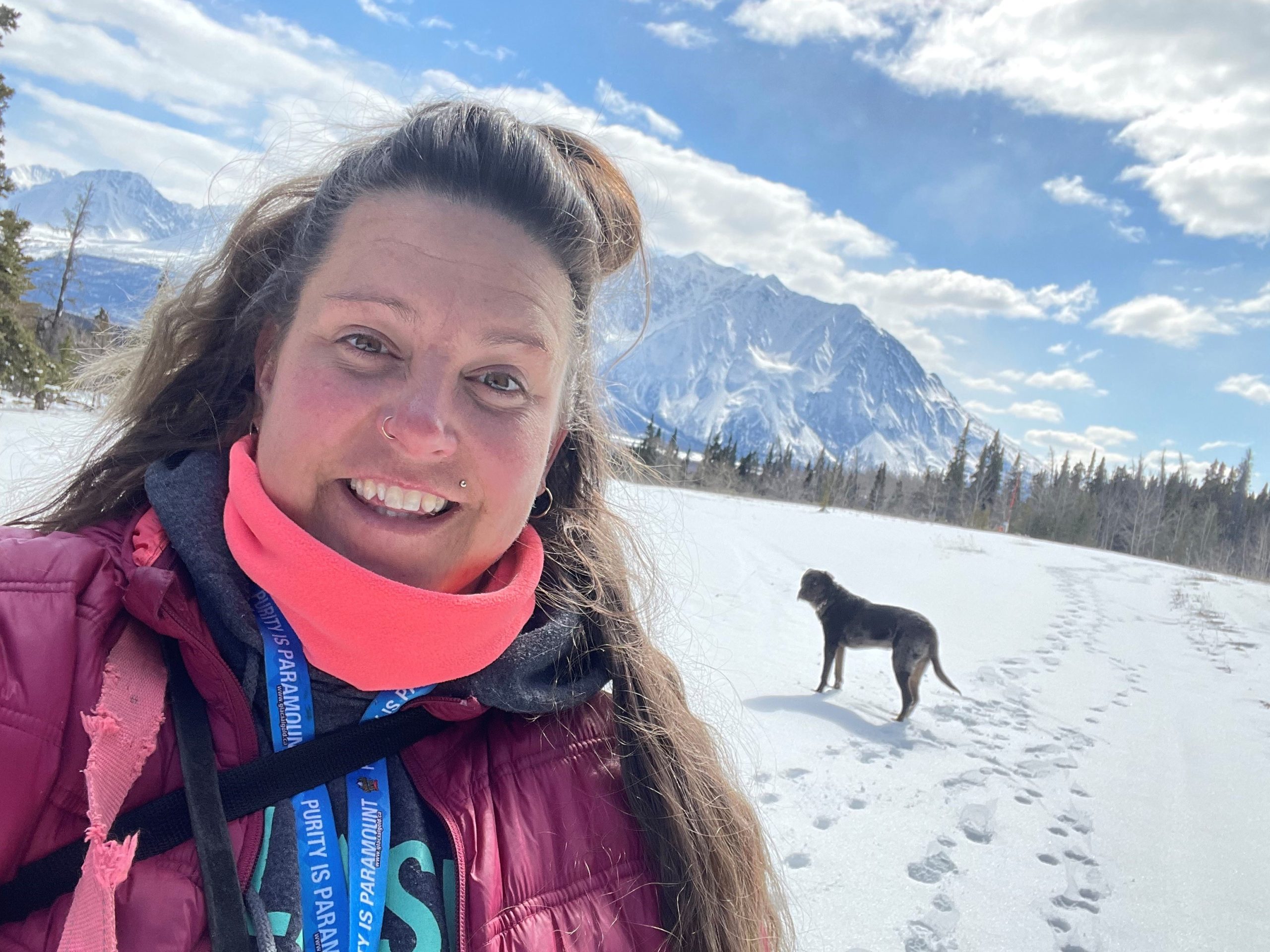 Isabelle Piché debout dans un champ enneigé, avec un chien et une montagne derrière elle. Isabelle Piché debout dans un champ enneigé, avec un chien et une montagne derrière elle.