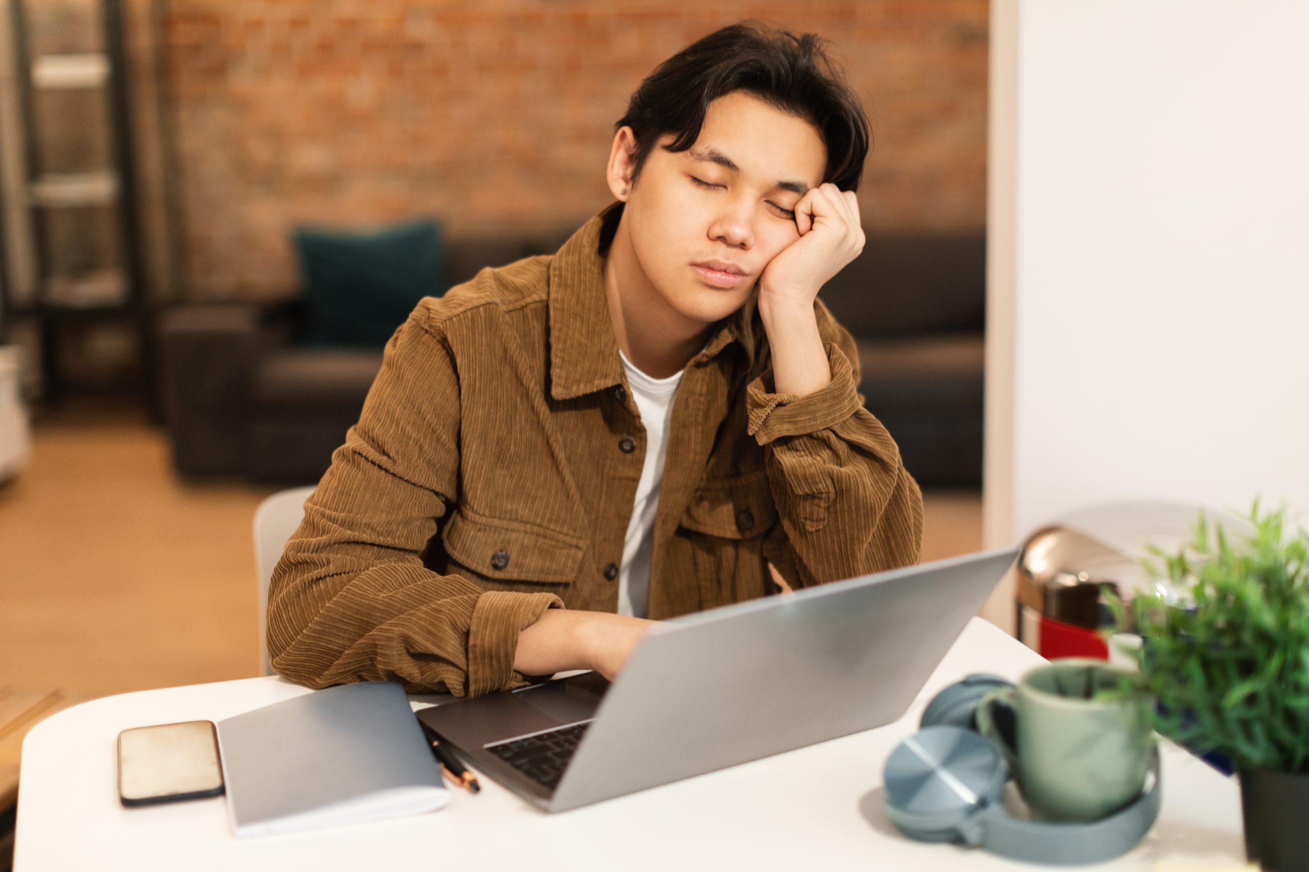 A man sleeping in front of a laptop at a desk. A man sleeping in front of a laptop at a desk.