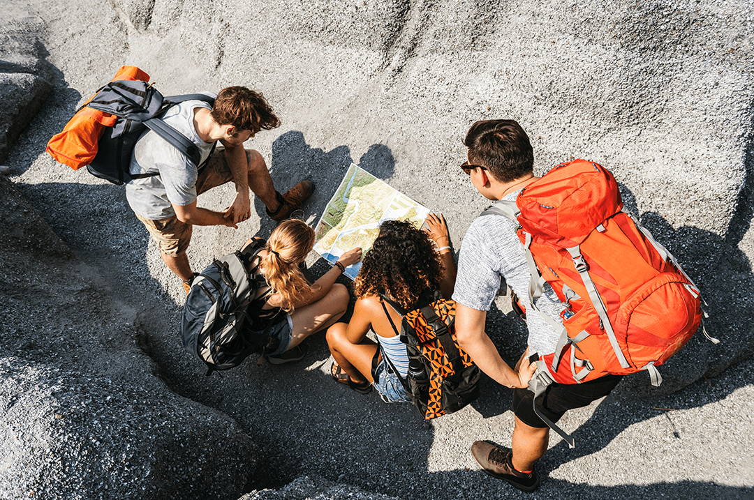 A group on a hiking trip gathering around and discussing their route on a map A group on a hiking trip gathering around and discussing their route on a map