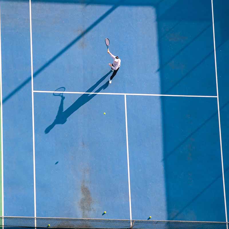 overhead view of a person hitting a ball on a tennis court with their racket overhead view of a person hitting a ball on a tennis court with their racket