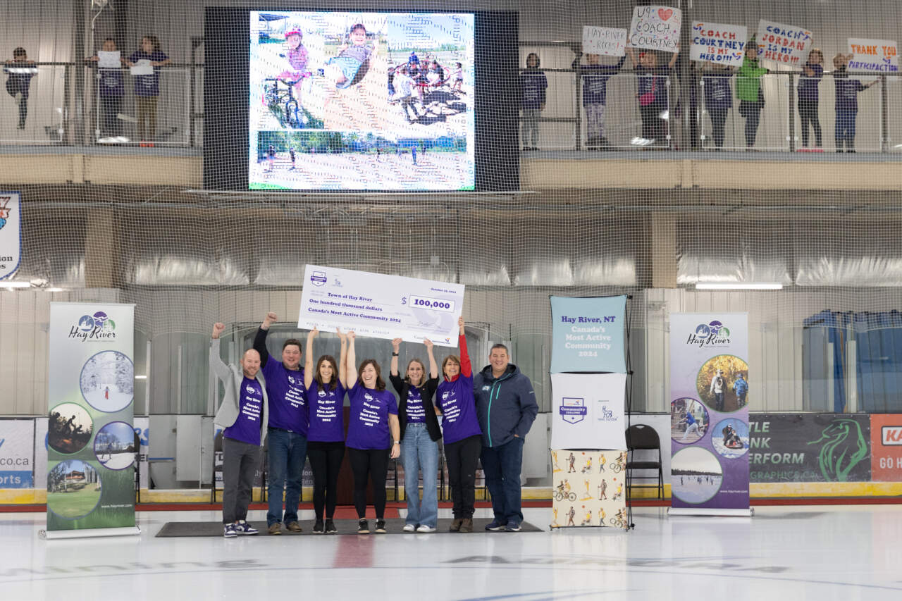 Hay River community residents holding up a large $100,000 cheque on an ice rink Hay River community residents holding up a large $100,000 cheque on an ice rink