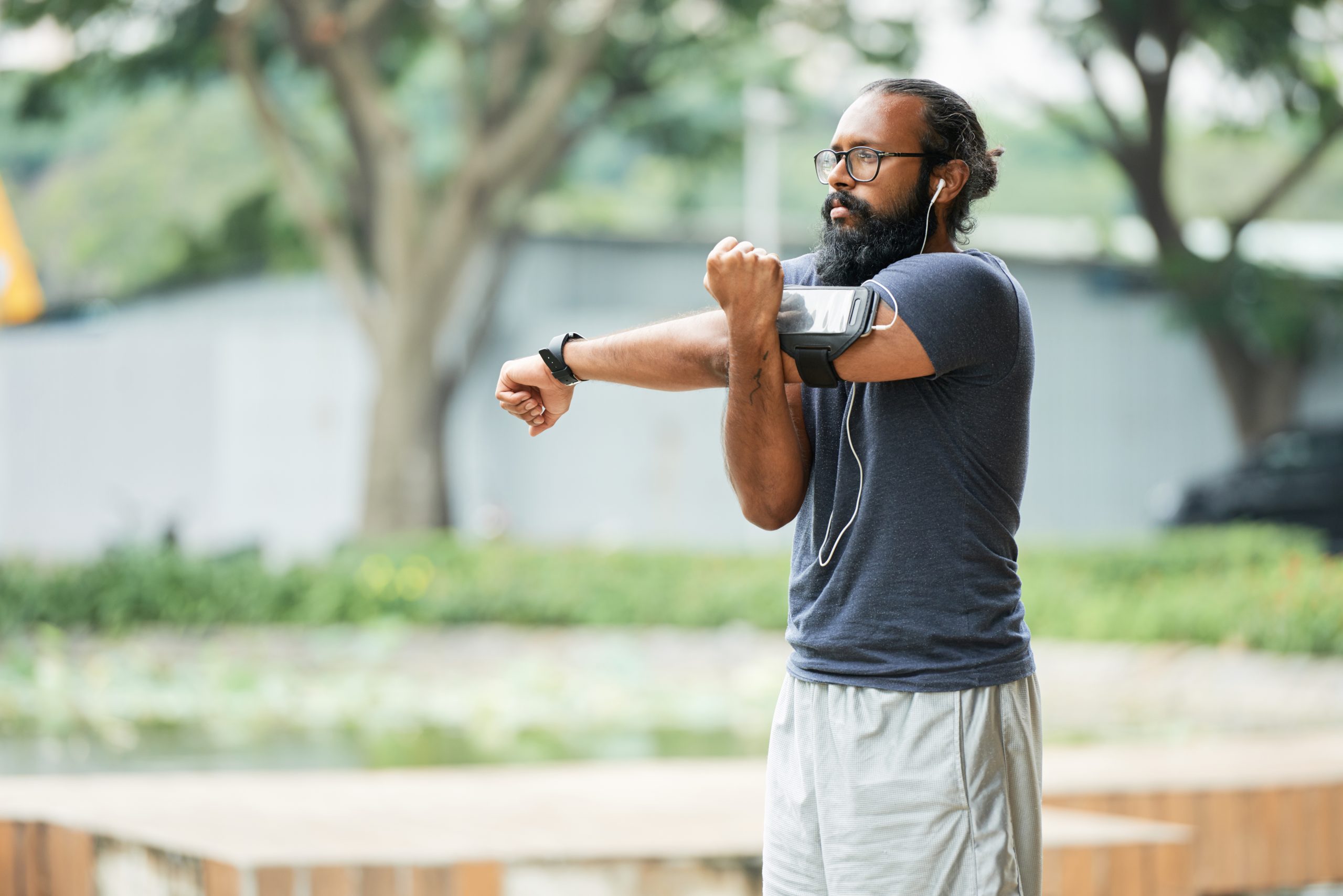 A man with a fitness tracker on his wrist stretching his arm at a park. A man with a fitness tracker on his wrist stretching his arm at a park.