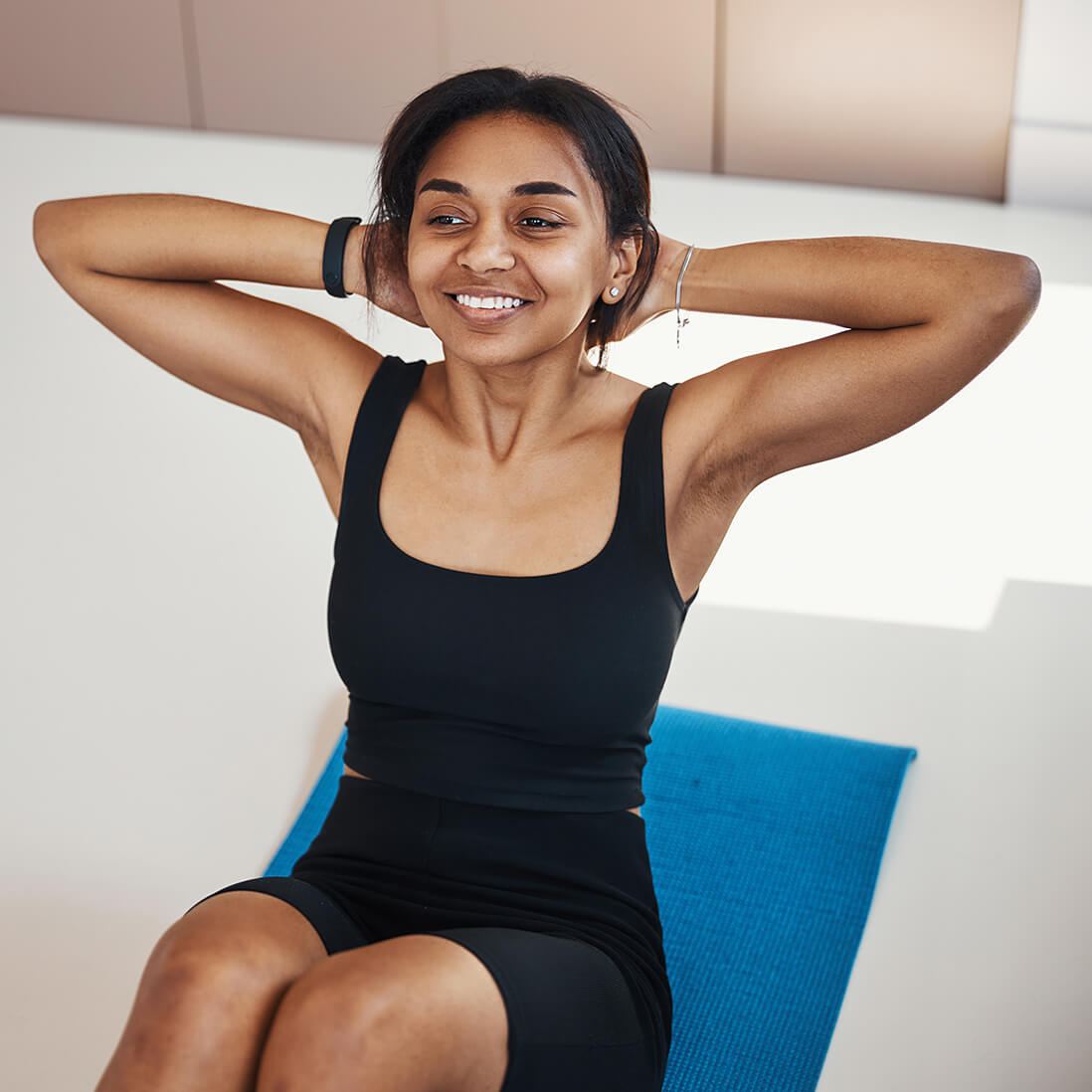Une femme souriante fait des redressements assis sur un tapis de yoga.