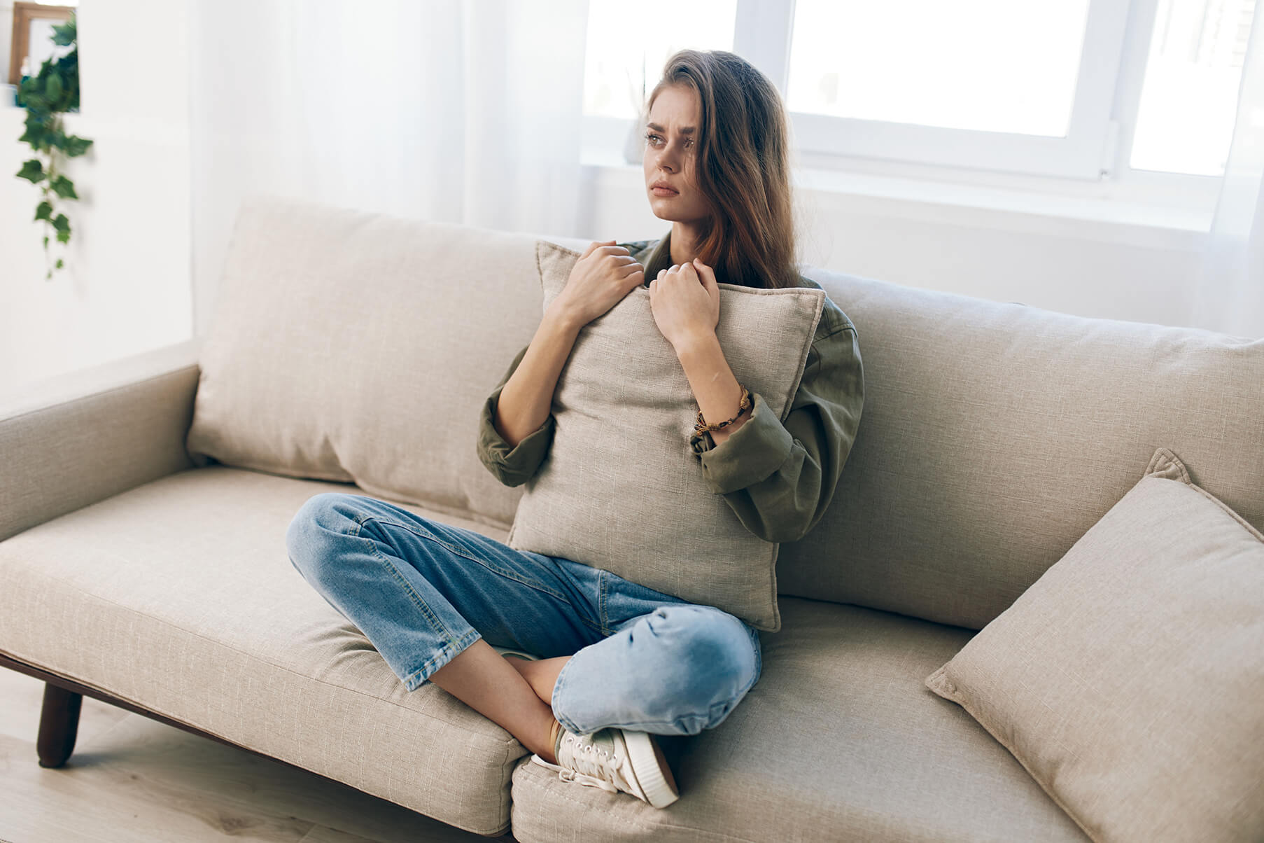 Une femme serre un oreiller assise les jambes croisées sur un divan. Une femme serre un oreiller assise les jambes croisées sur un divan.