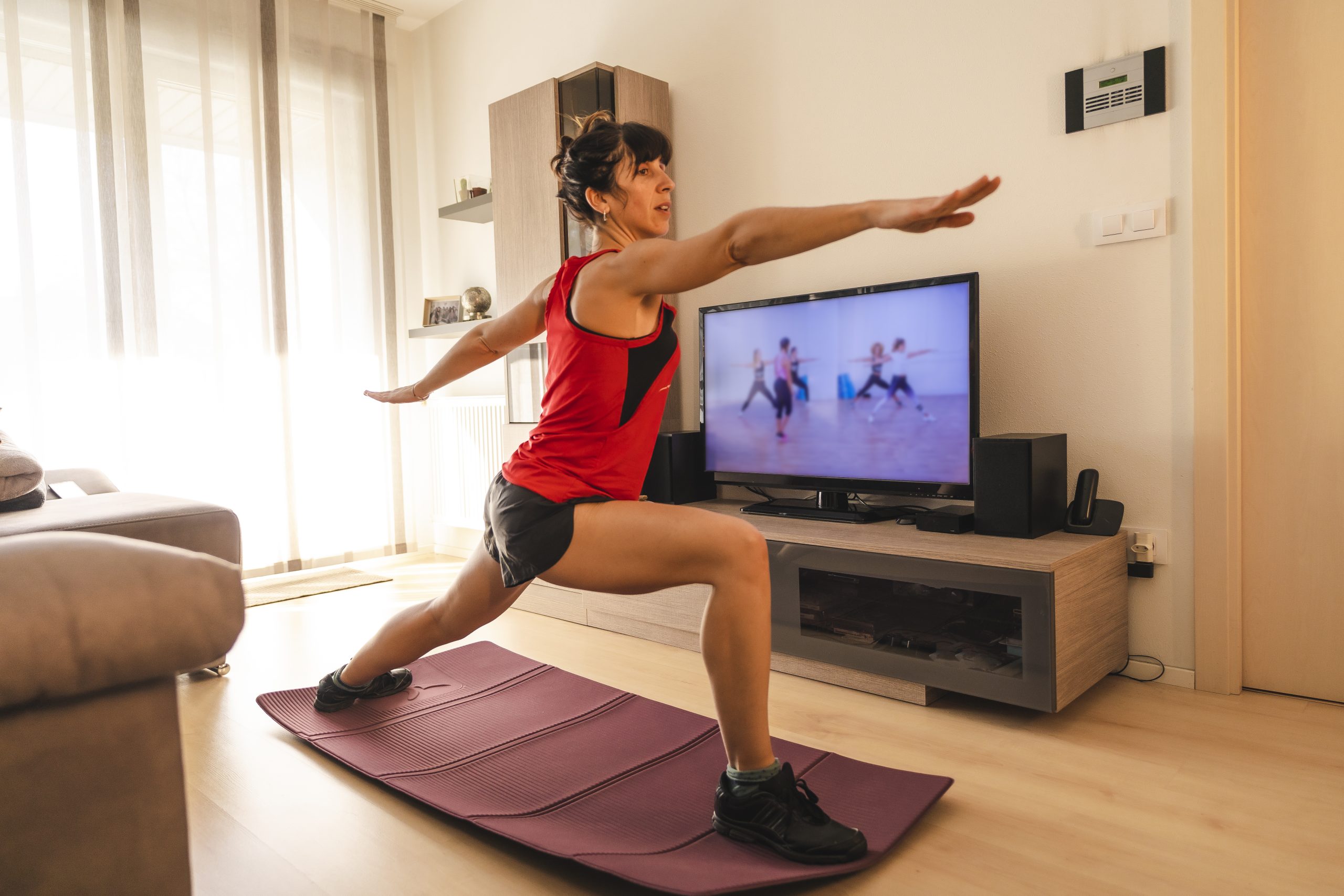 A woman doing yoga in front of a TV displaying a workout video. A woman doing yoga in front of a TV displaying a workout video.
