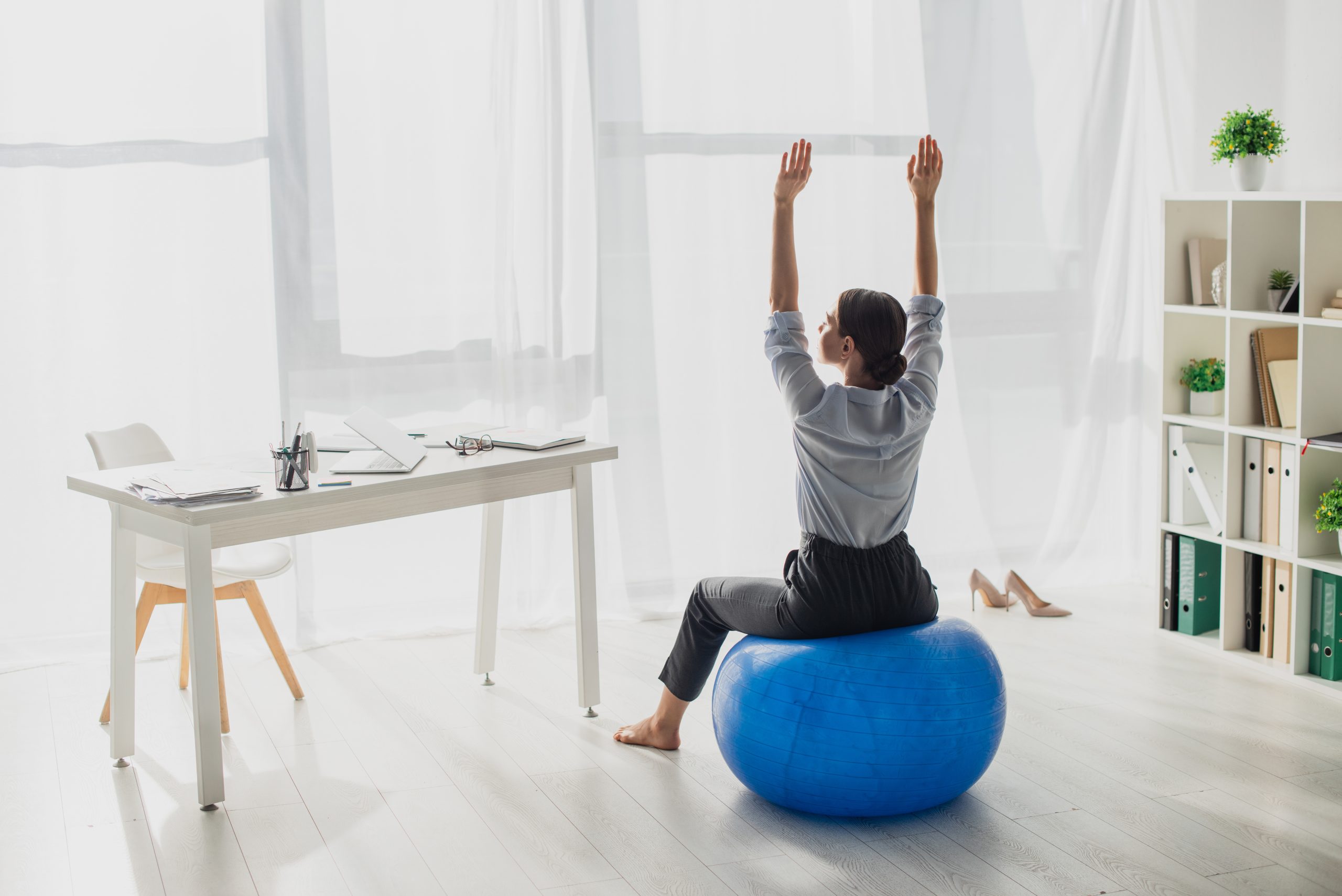 A woman stretching her arms over her head while sitting on a stability ball in an office. A woman stretching her arms over her head while sitting on a stability ball in an office.