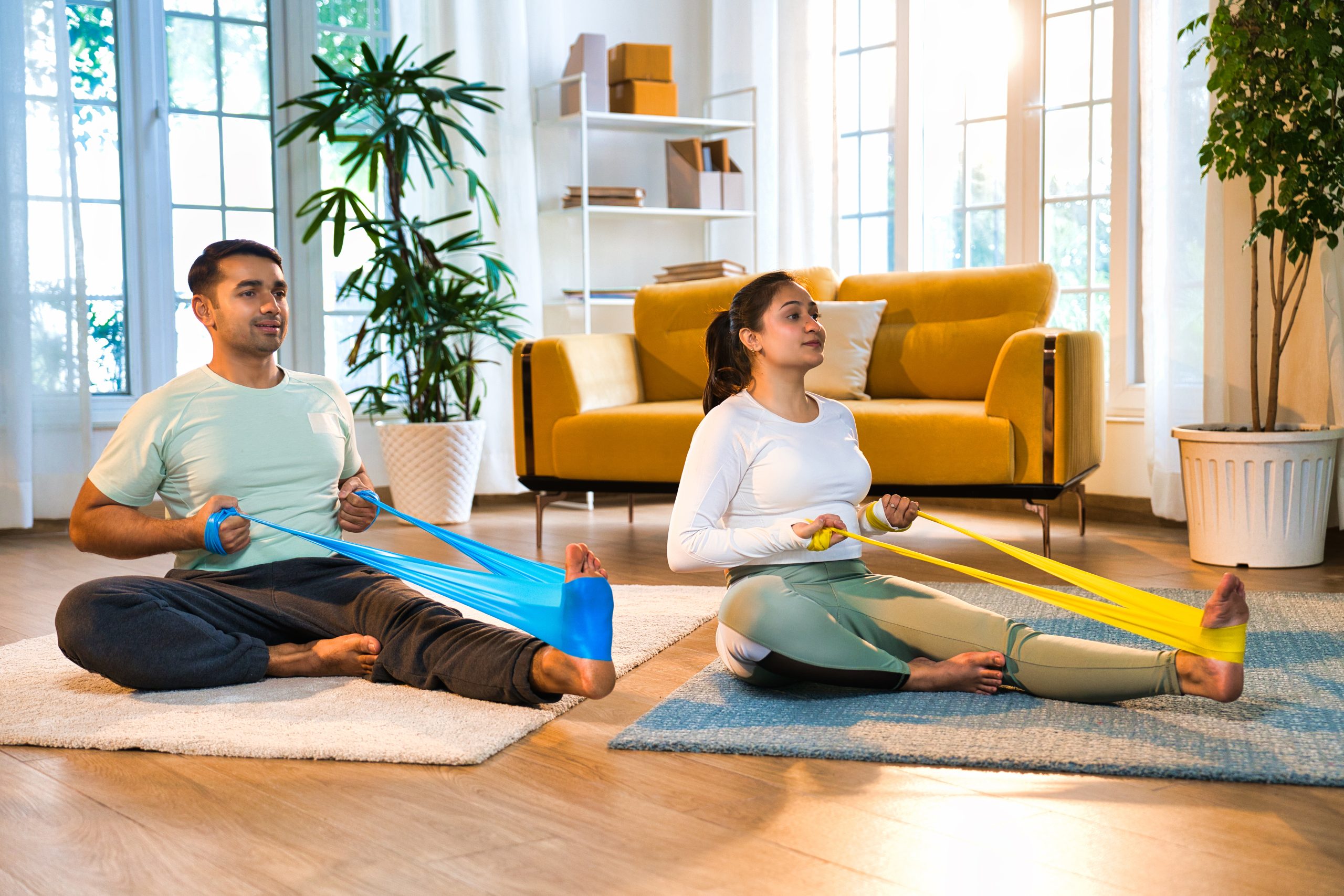 A man and woman exercising with resistance bands on the floor of a living room. A man and woman exercising with resistance bands on the floor of a living room.