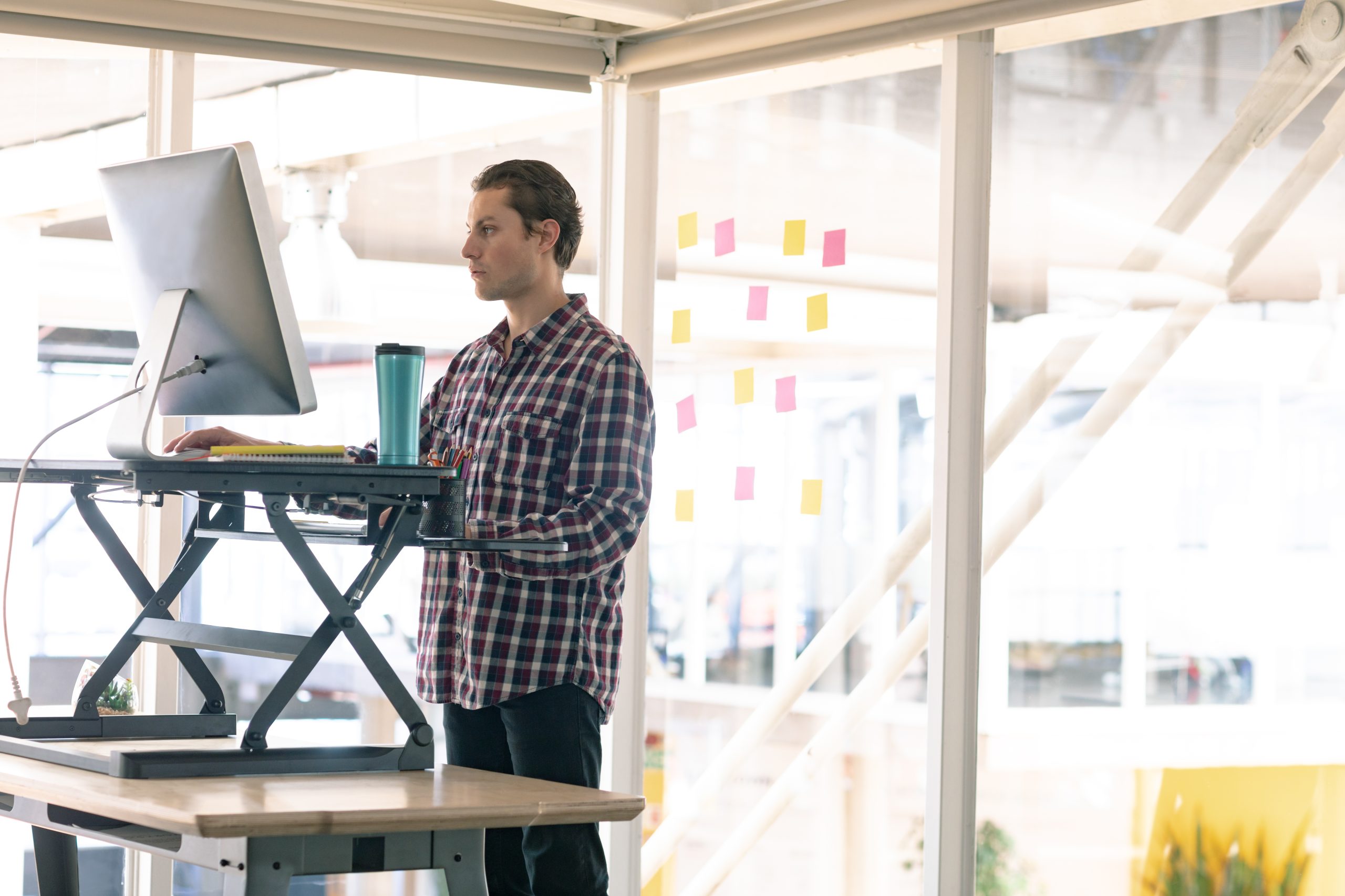A man standing in front of a computer placed on an adjustable standing desk. A man standing in front of a computer placed on an adjustable standing desk.