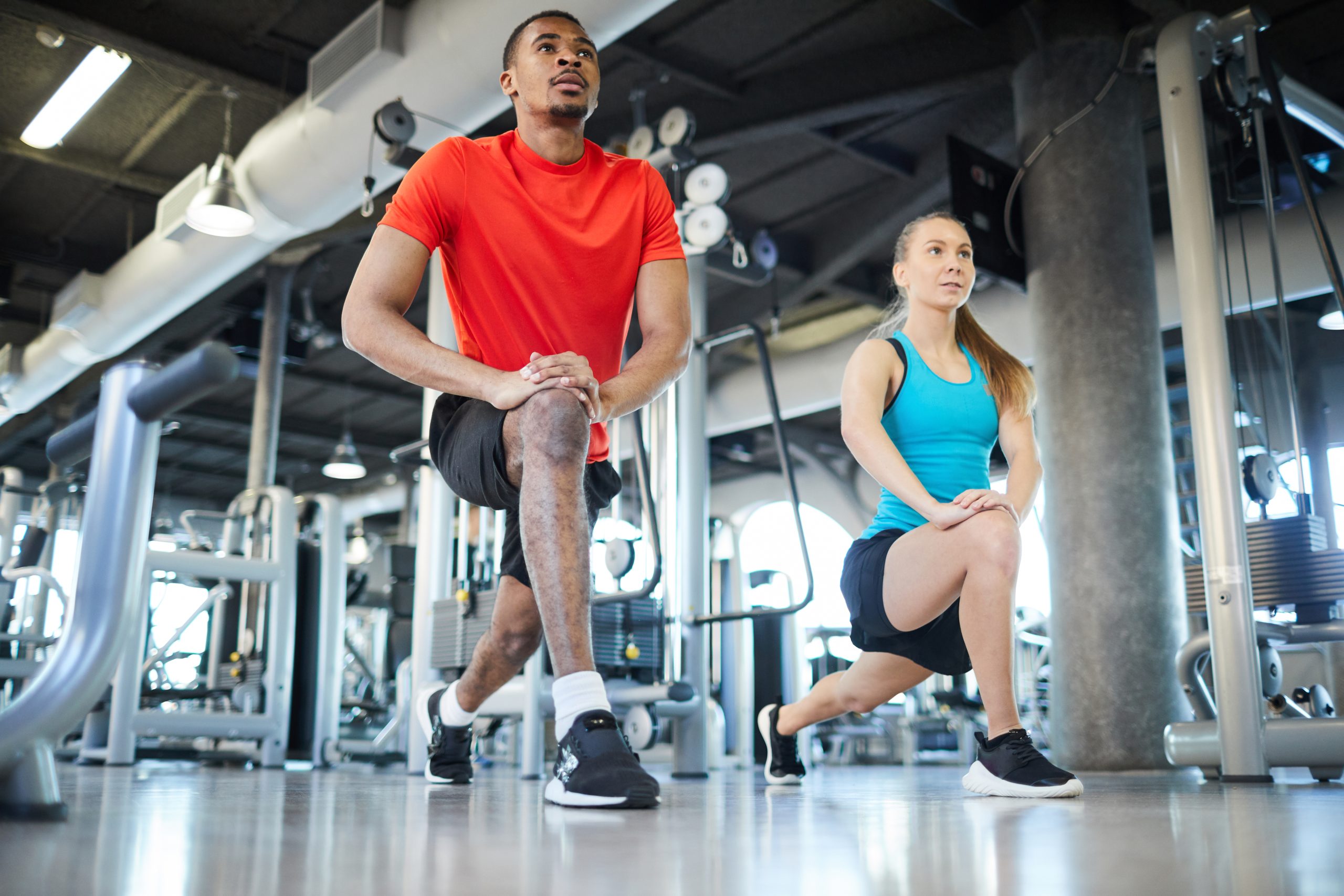 A man and woman doing lunges at a gym. A man and woman doing lunges at a gym.