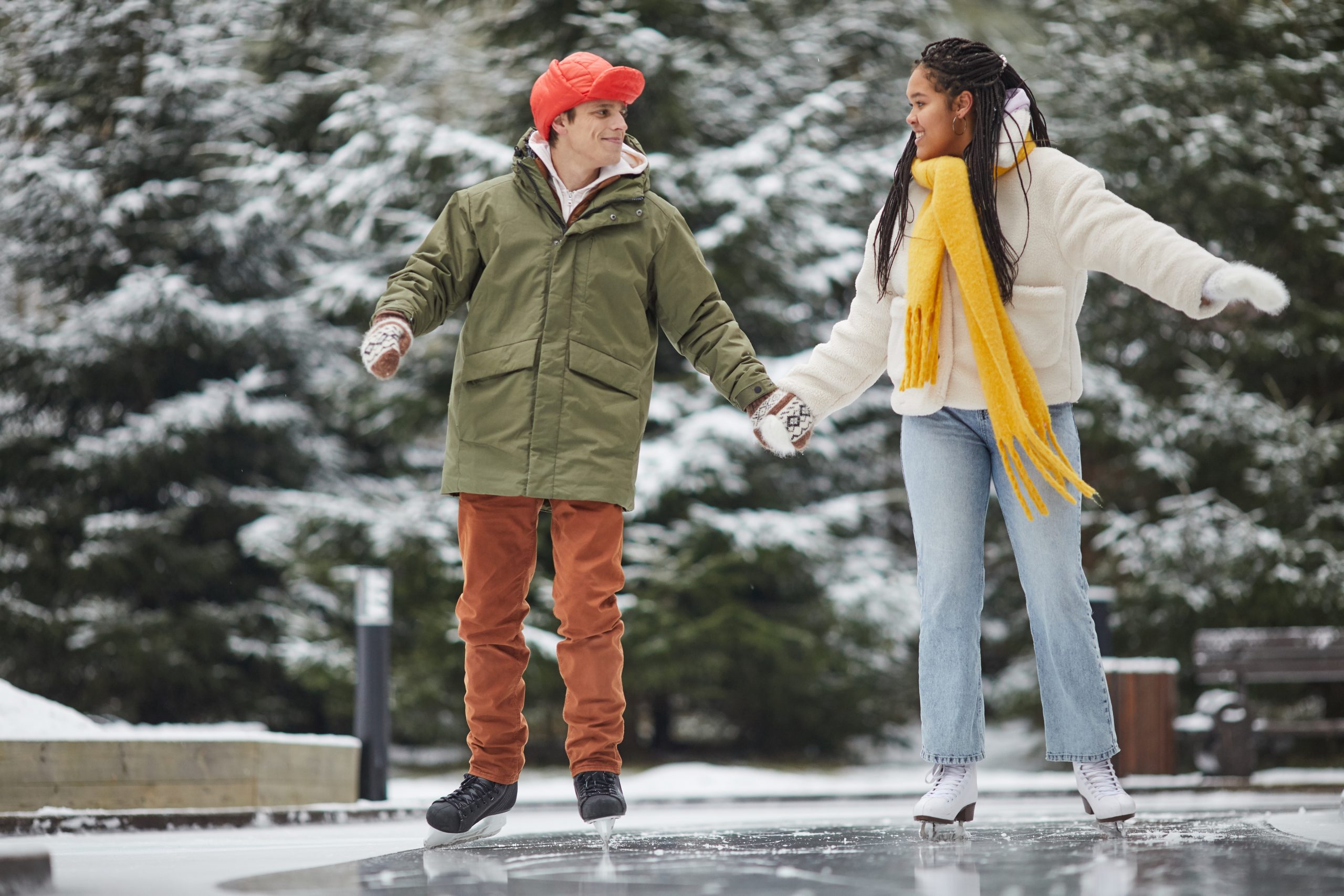 Un homme et une femme patinent sur une patinoire extérieure entourée d’arbres. Un homme et une femme patinent sur une patinoire extérieure entourée d’arbres.