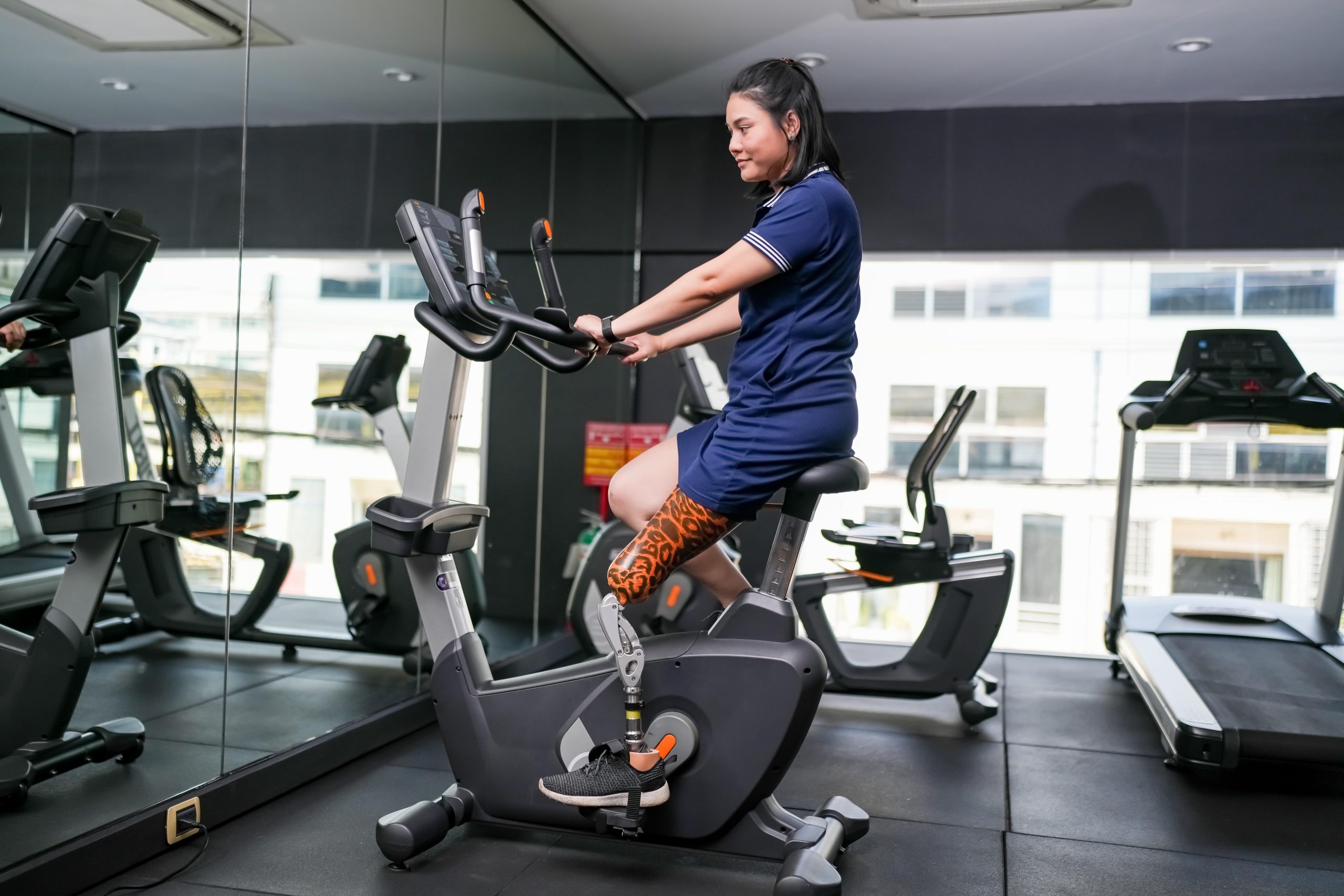 Une femme avec une prothèse de jambe pédale sur un vélo stationnaire dans un gym. Une femme avec une prothèse de jambe pédale sur un vélo stationnaire dans un gym.