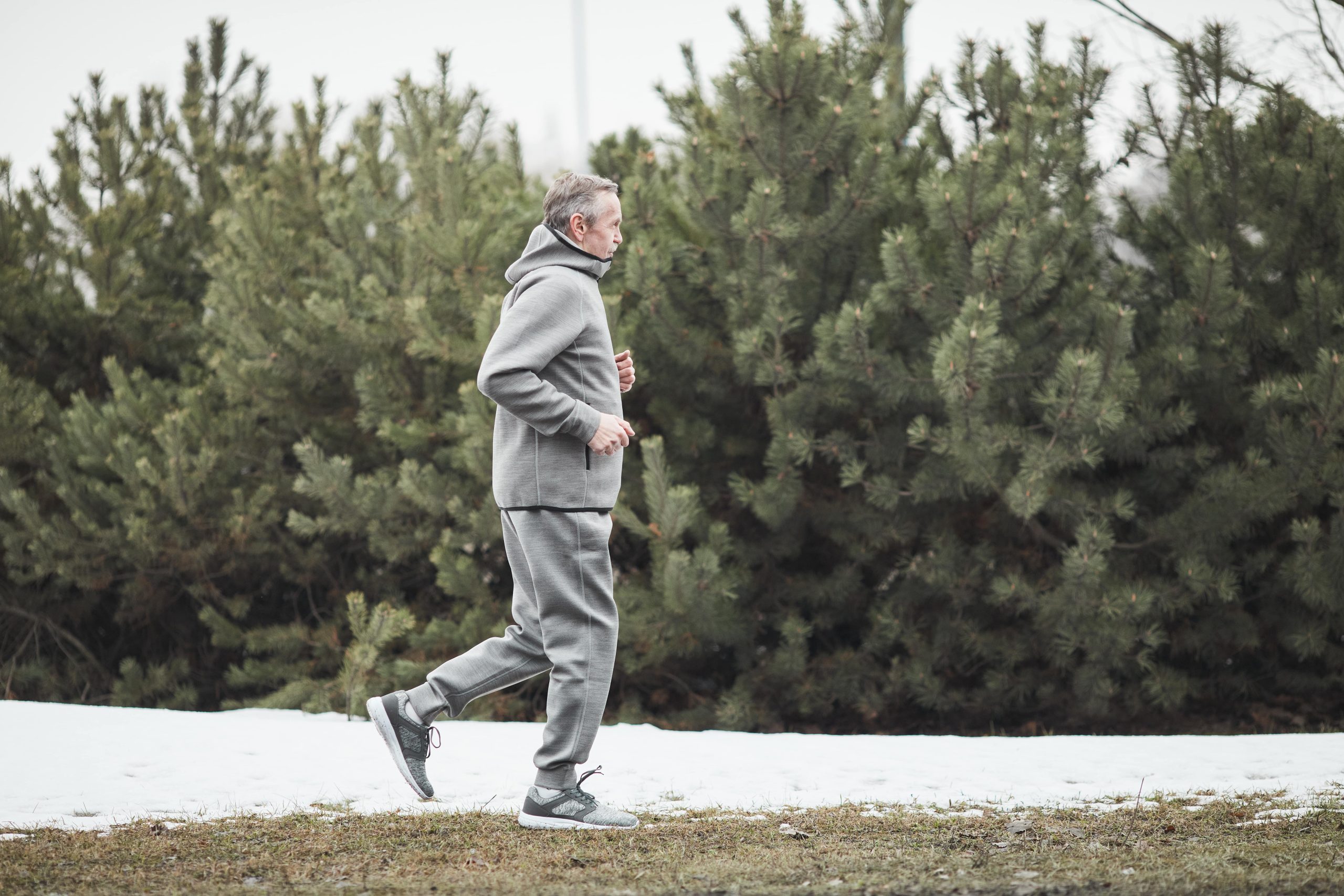Un homme fait du jogging dans la neige devant une haie de conifères. Un homme fait du jogging dans la neige devant une haie de conifères.