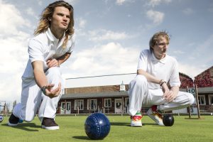 Two young men playing a game of bowls.