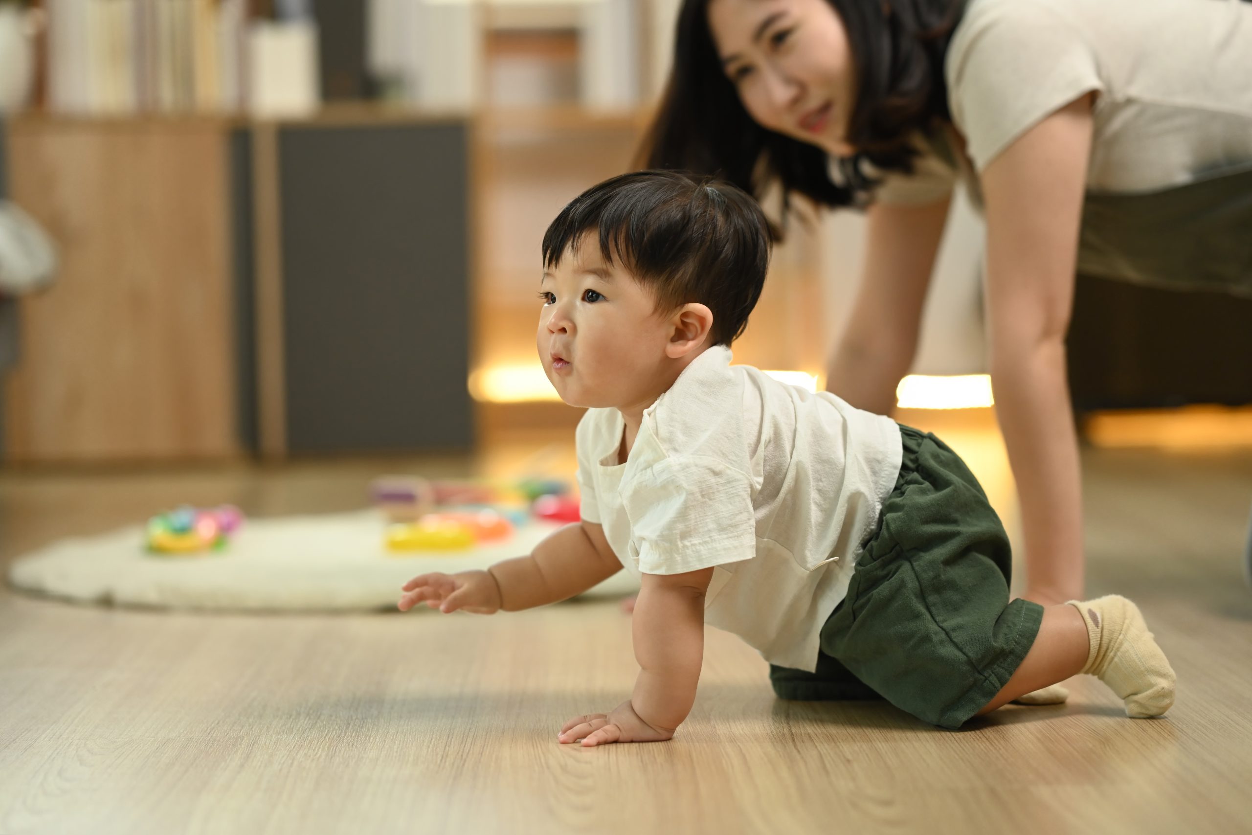 Un bébé garçon rampe sur le sol du salon sous le regard de sa mère. Un bébé garçon rampe sur le sol du salon sous le regard de sa mère.