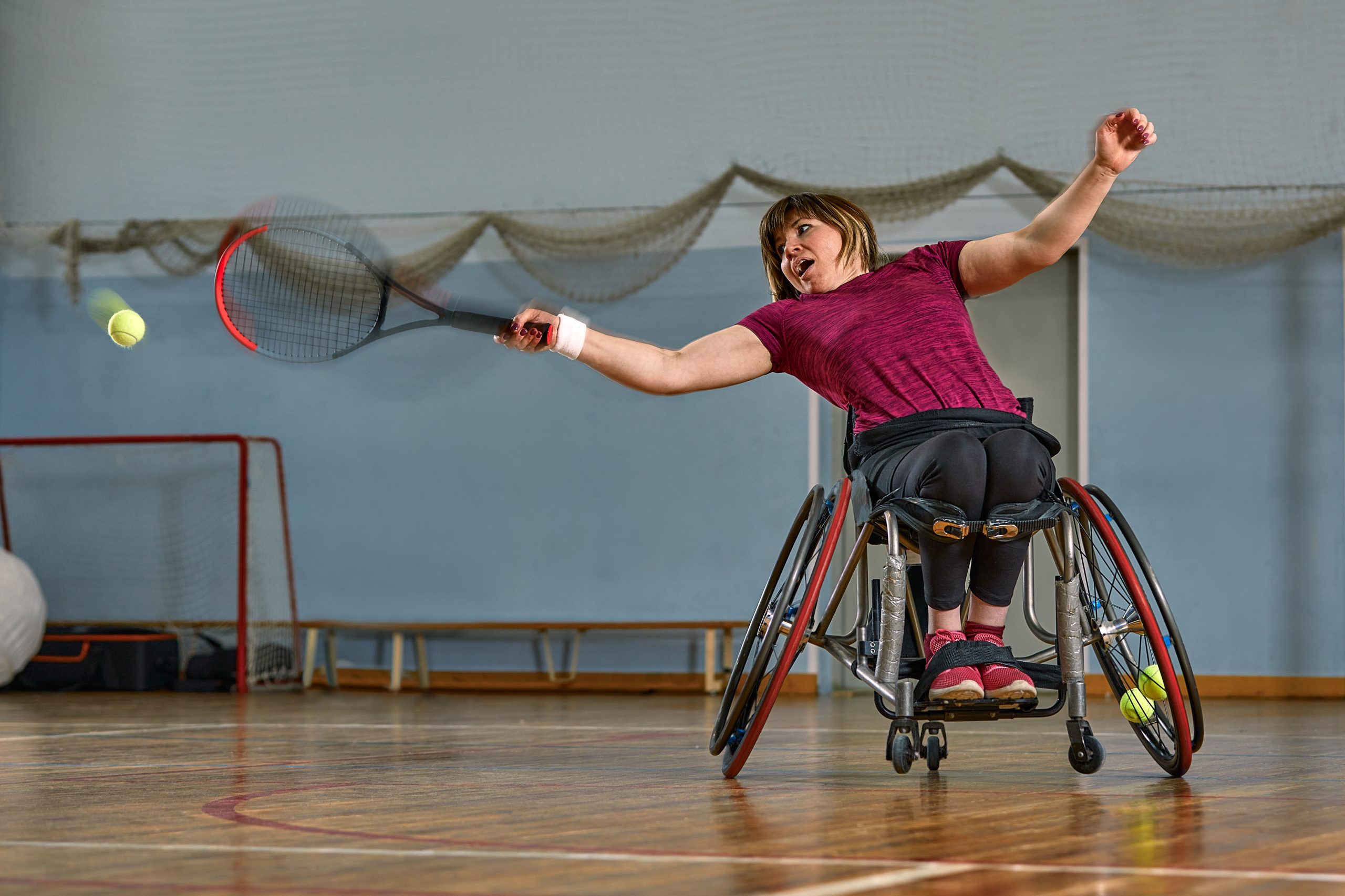 Un femme en fauteuil roulant joue au tennis dans un gymnase. Un femme en fauteuil roulant joue au tennis dans un gymnase.
