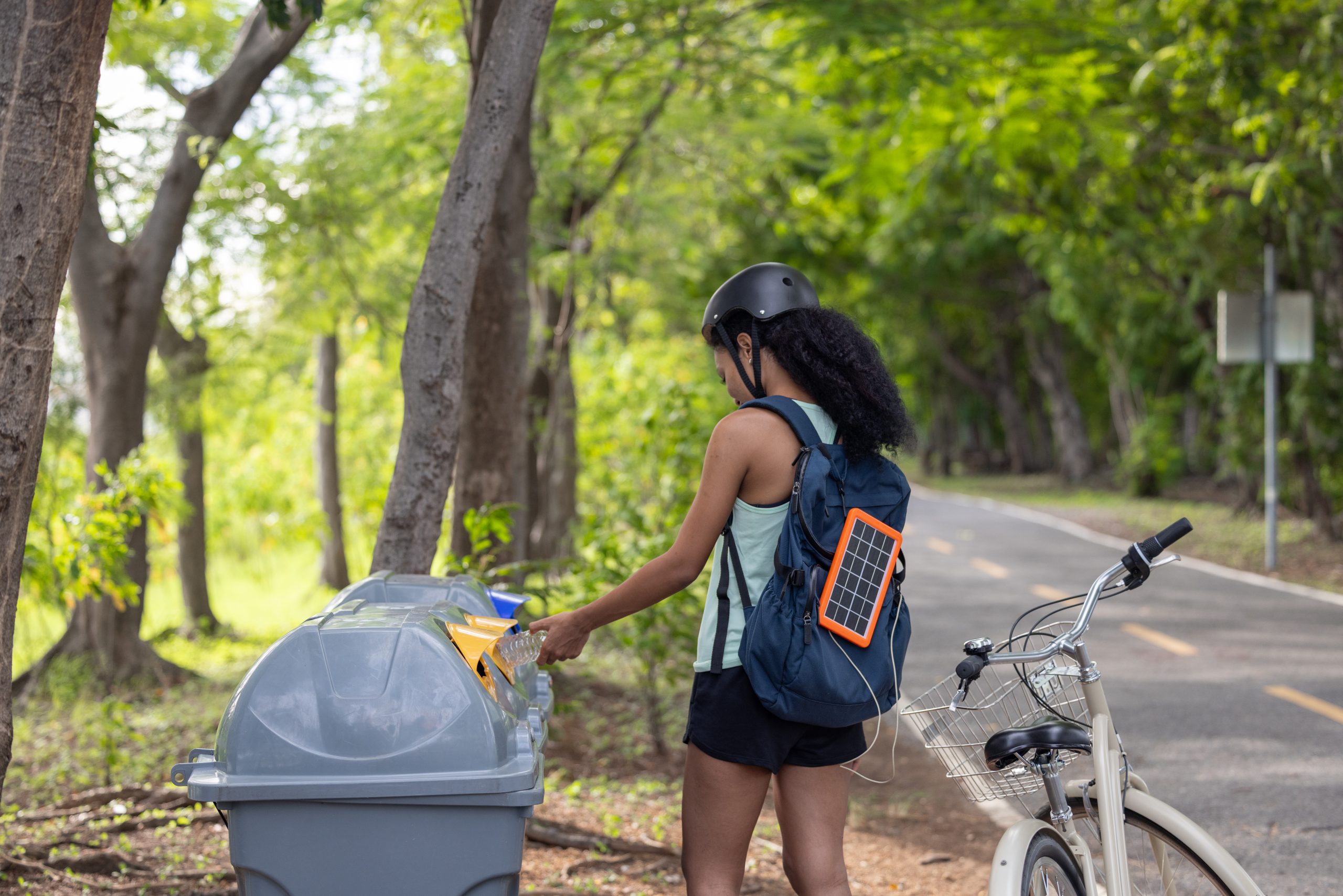 A cyclist placing a plastic bottle into a trash bin on the side of the road. A cyclist placing a plastic bottle into a trash bin on the side of the road.