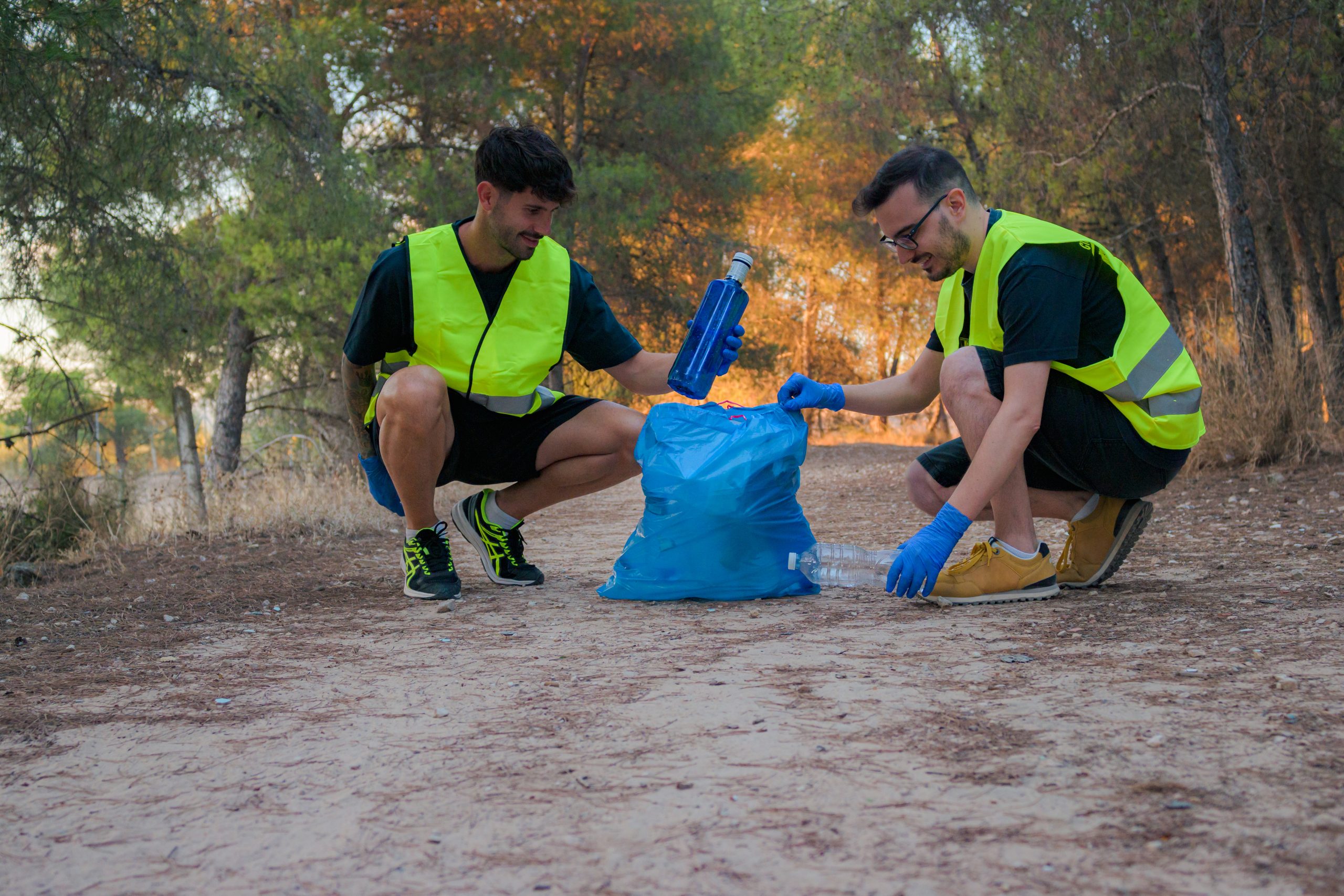 Two men in vests picking up trash on a hiking trail. Two men in vests picking up trash on a hiking trail.