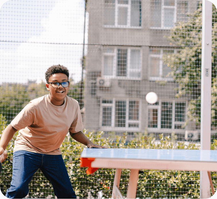 Un adolescent joue au tennis de table à l’extérieur dans un parc.