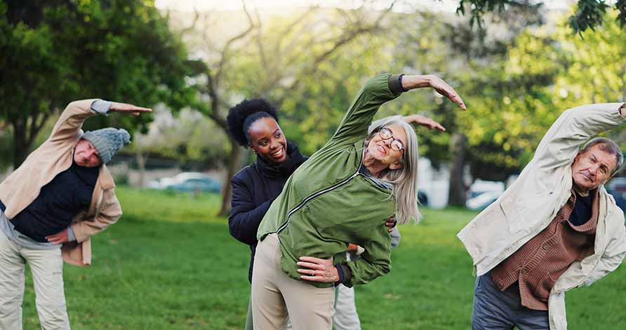 A group of older adults stretching at a park. A group of older adults stretching at a park.
