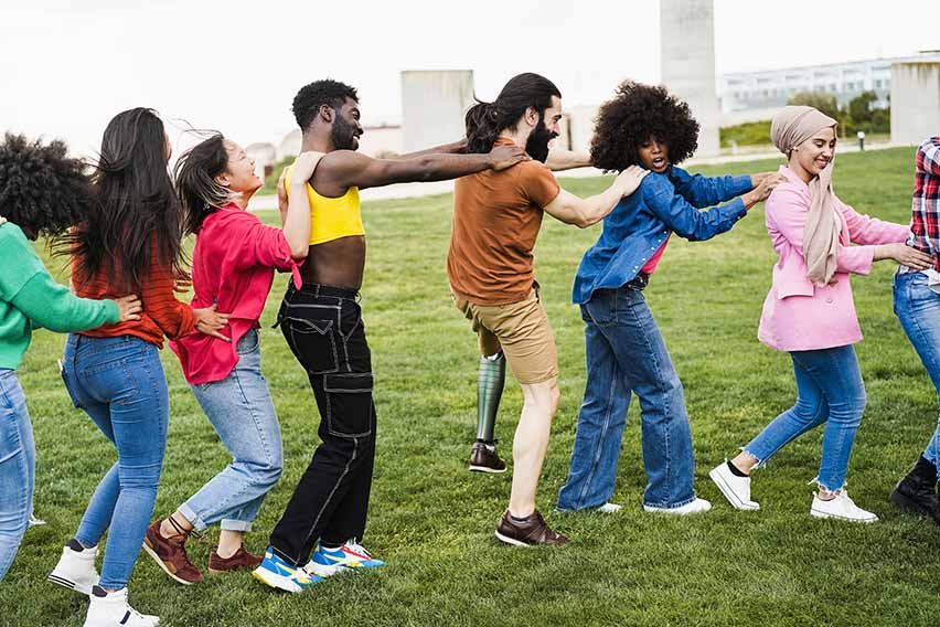 A group of young adults in a conga line at a park. A group of young adults in a conga line at a park.
