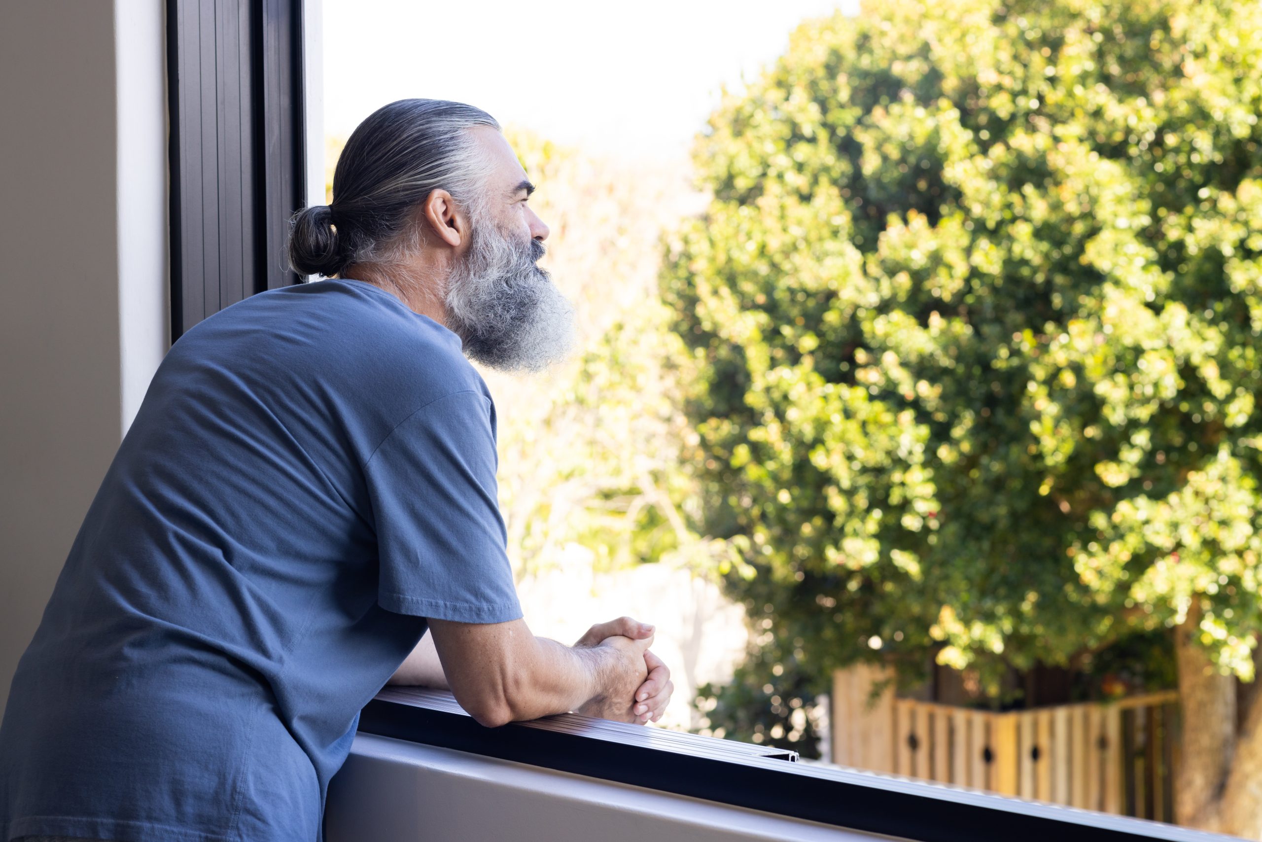 A man looking out a window on a sunny day. 