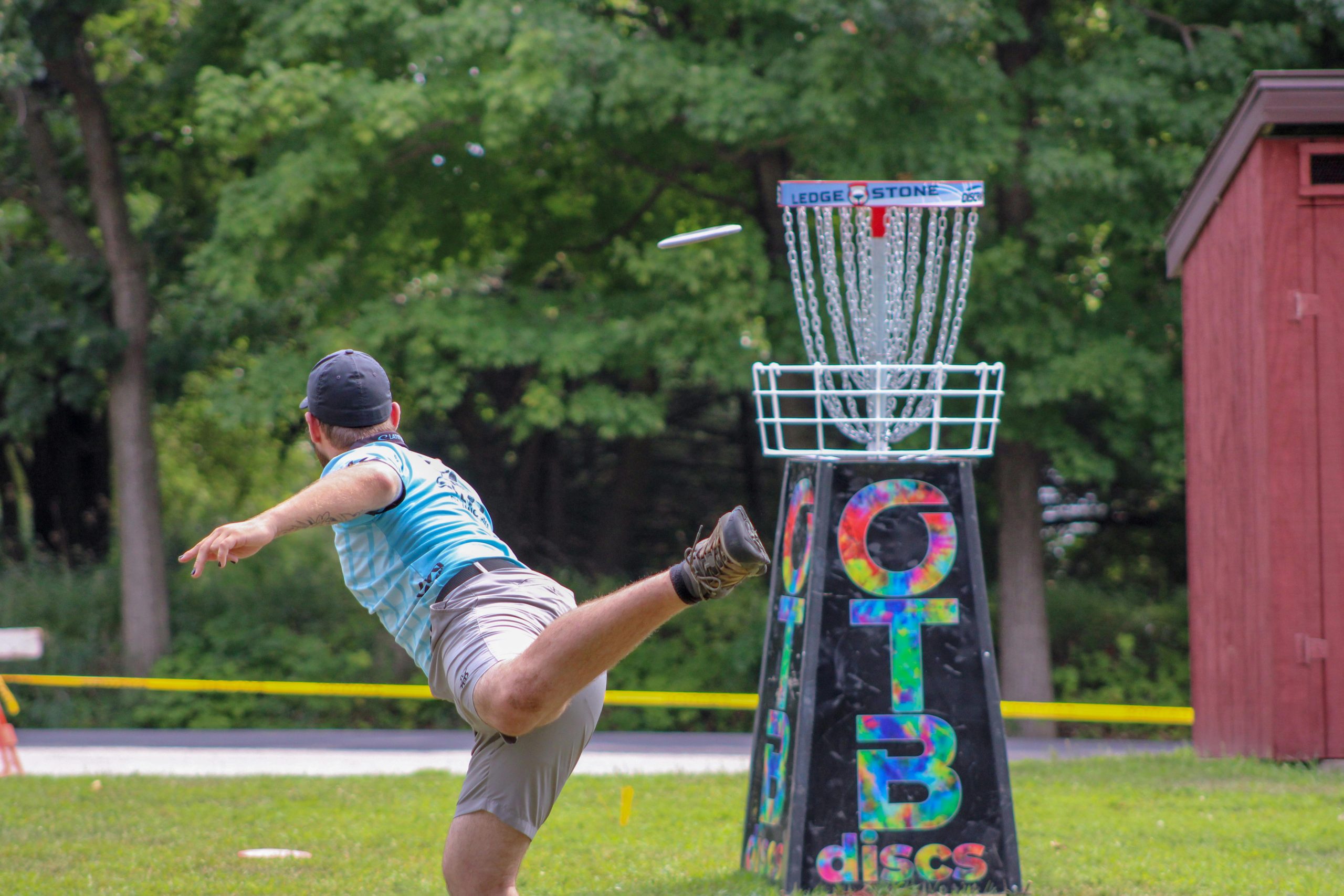 Sur un terrain de disc-golf, un homme lance un disque vers un panier cible. 