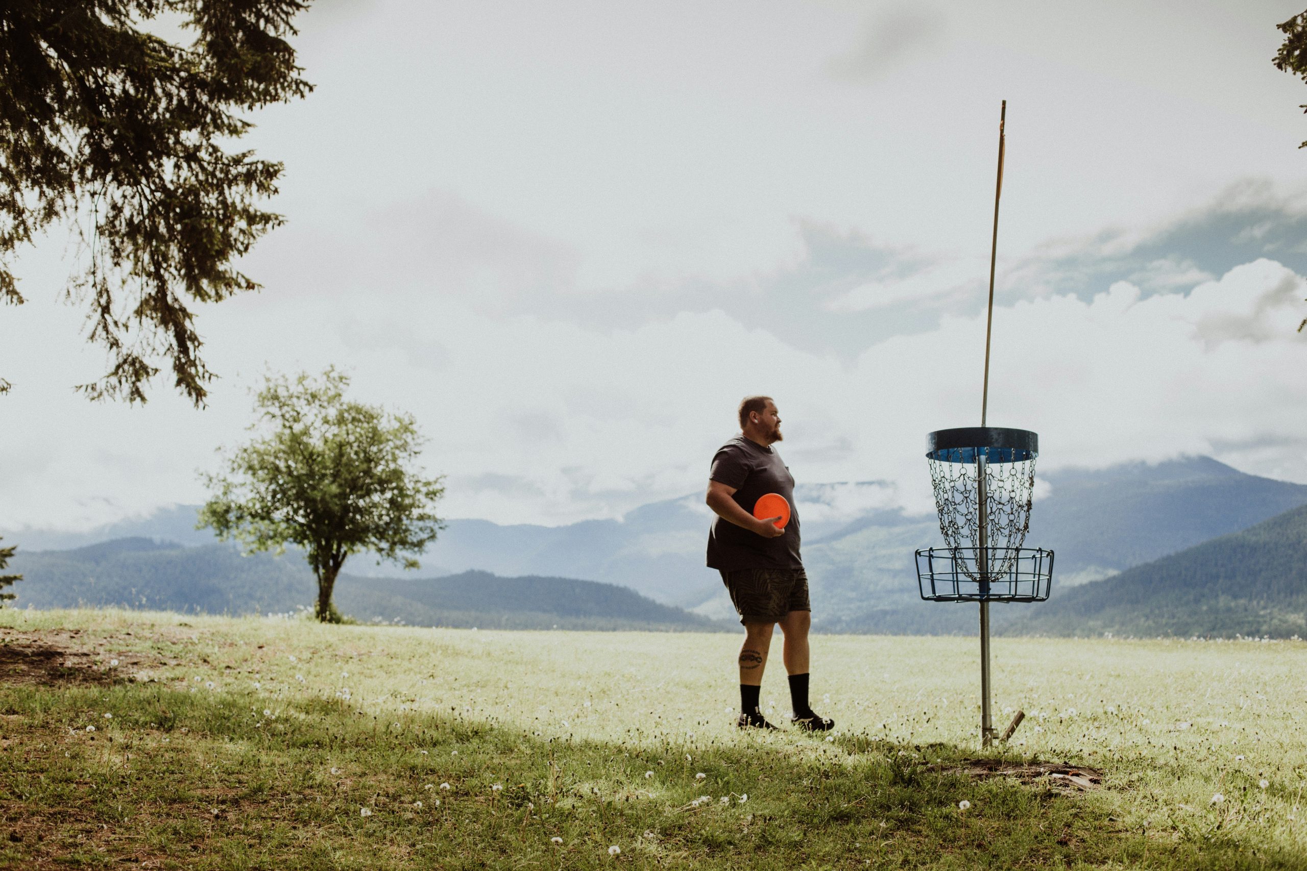 A man holding a plastic disc on a field beside a disc golf course basket target.