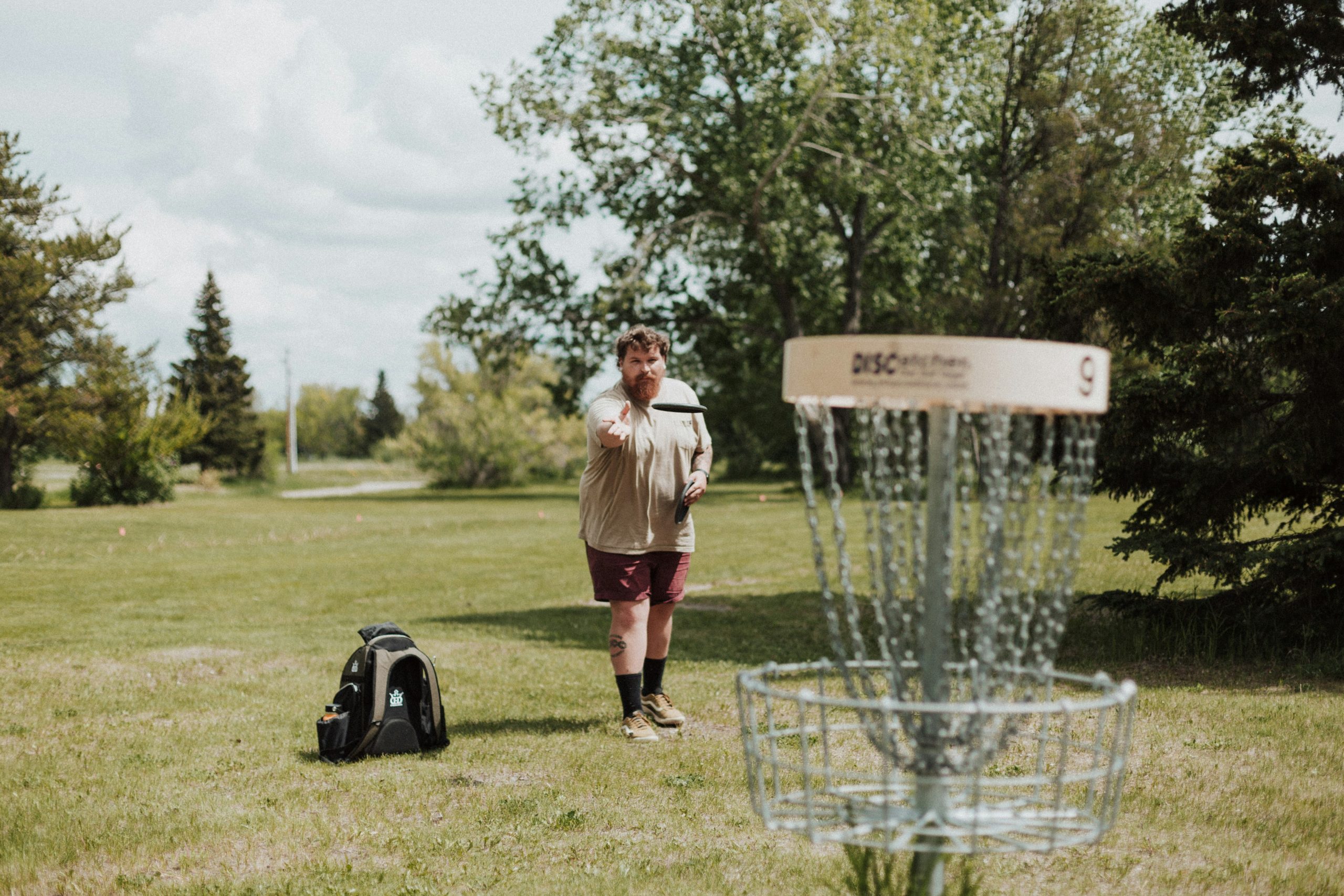 A man throwing a disc at a disc golf course basket target.  