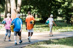 A group of older adults holding yoga mats while walking on a park path.