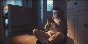 A man in exercise clothes sitting on the floor while looking at a smartphone.