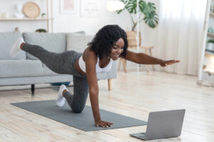 Une femme fait du yoga devant un ordinateur portable dans un salon.