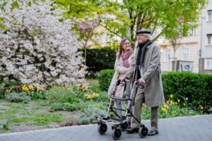 Une femme marchant à côté d’un homme âgé qui utilise un déambulateur sur un trottoir.